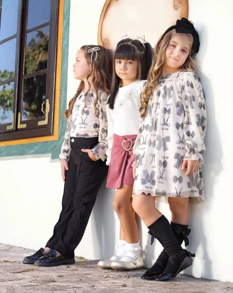 Três crianças usando roupas da coleção Lilo & Bela, em look elegante com vestido estampado, calça social e sapato